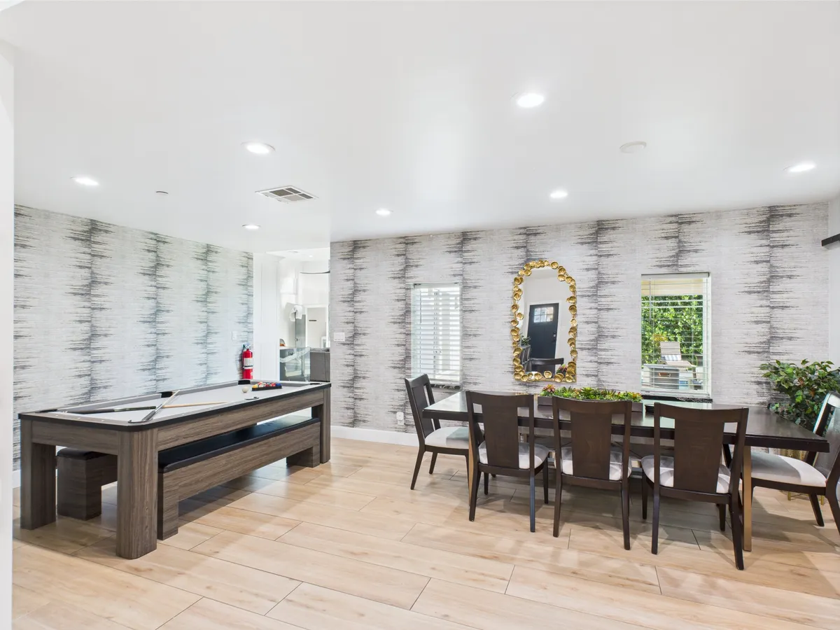 A stylish interior shot showcasing a well-equipped game room with a pool table, elegant dining area, decorative mirror, and textured wallpaper. The atmosphere is friendly and relaxed, inviting guests to enjoy after-golf socializing and leisure time indoors.