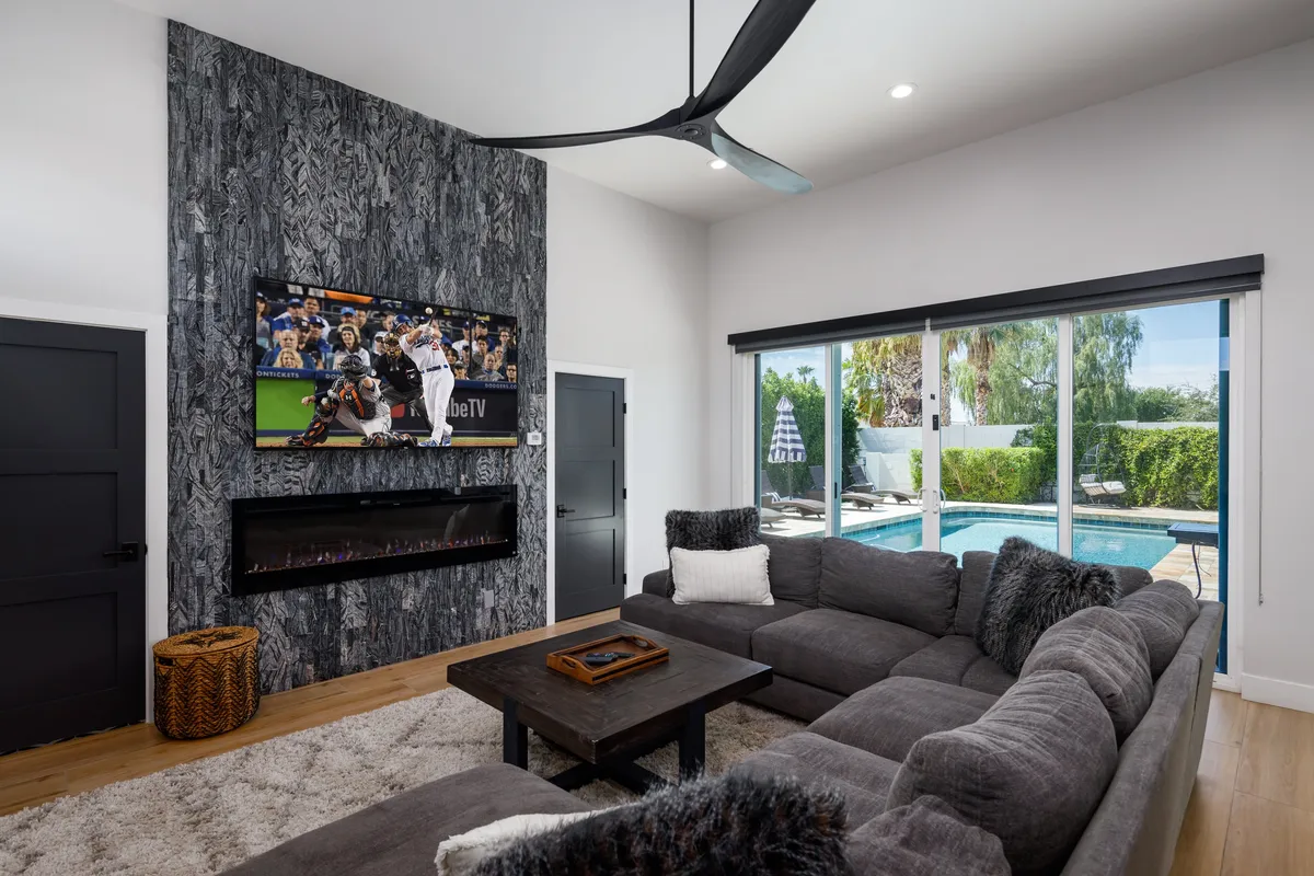 A welcoming media area with a large, comfortable sectional sofa, a modern flat-screen TV mounted on a textured stone wall, and an electric fireplace below. The room is accented by warm lighting and contemporary decor, inviting guests to gather for movie nights or casual conversation.