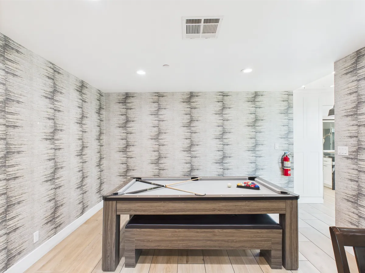 A modern, stylish interior game room with a sleek pool table as the focal point. Unique wall designs and statement lighting fixtures create an energetic, inviting setting perfect for friendly competition and shared laughter.