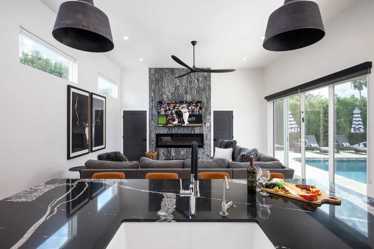A spacious, sociable layout seamlessly blending a large sectional sofa, a marble kitchen island, and a TV mounted above a fireplace. The room is artfully decorated, with the open-concept design supporting both group entertainment and relaxed lounging.