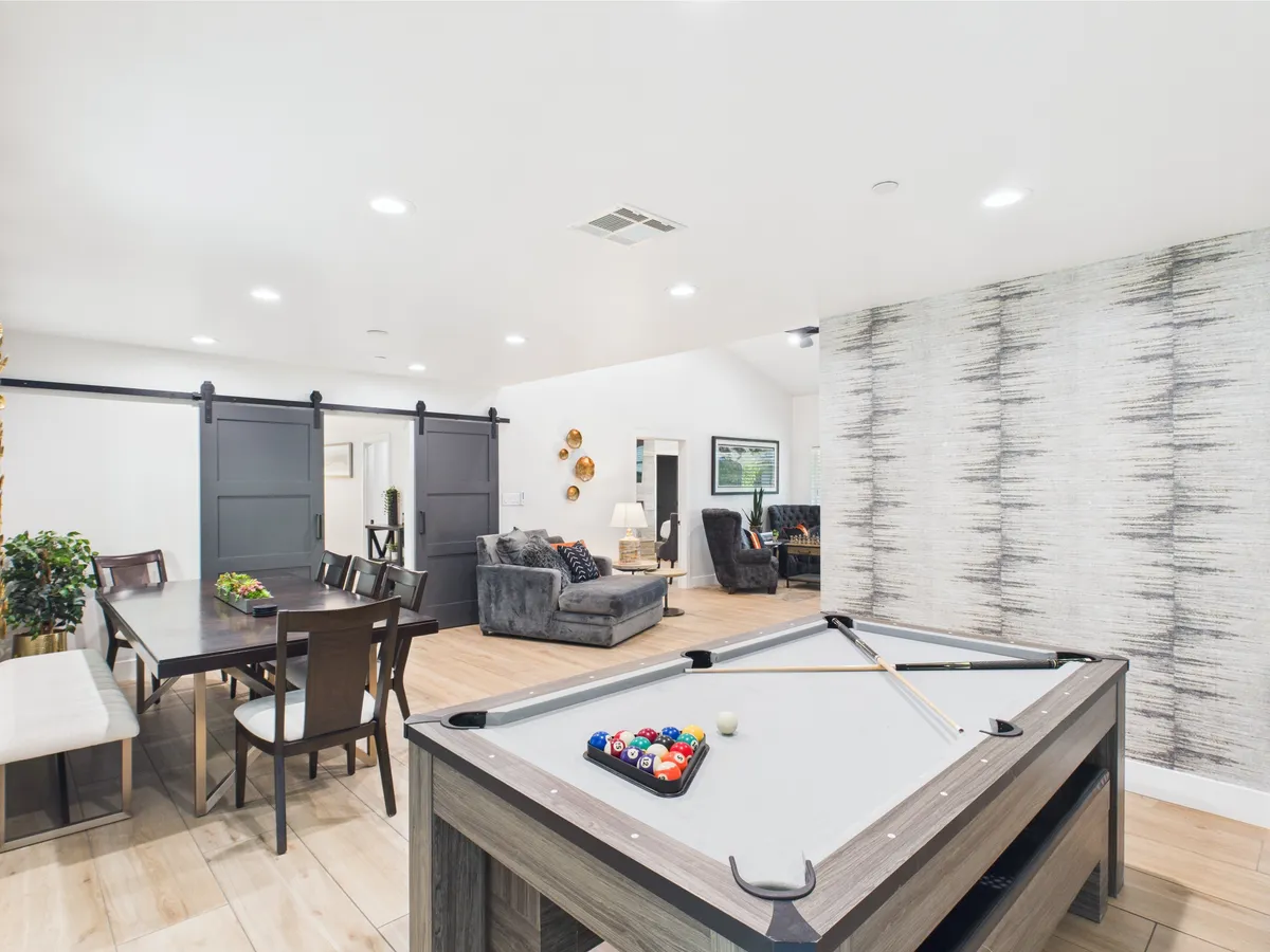 A friendly, lively game room scene featuring a pool table, dining table, and a comfortable seating area set against a decorative wall. The layout encourages group gatherings and social interaction, perfect for both casual play and family game nights.