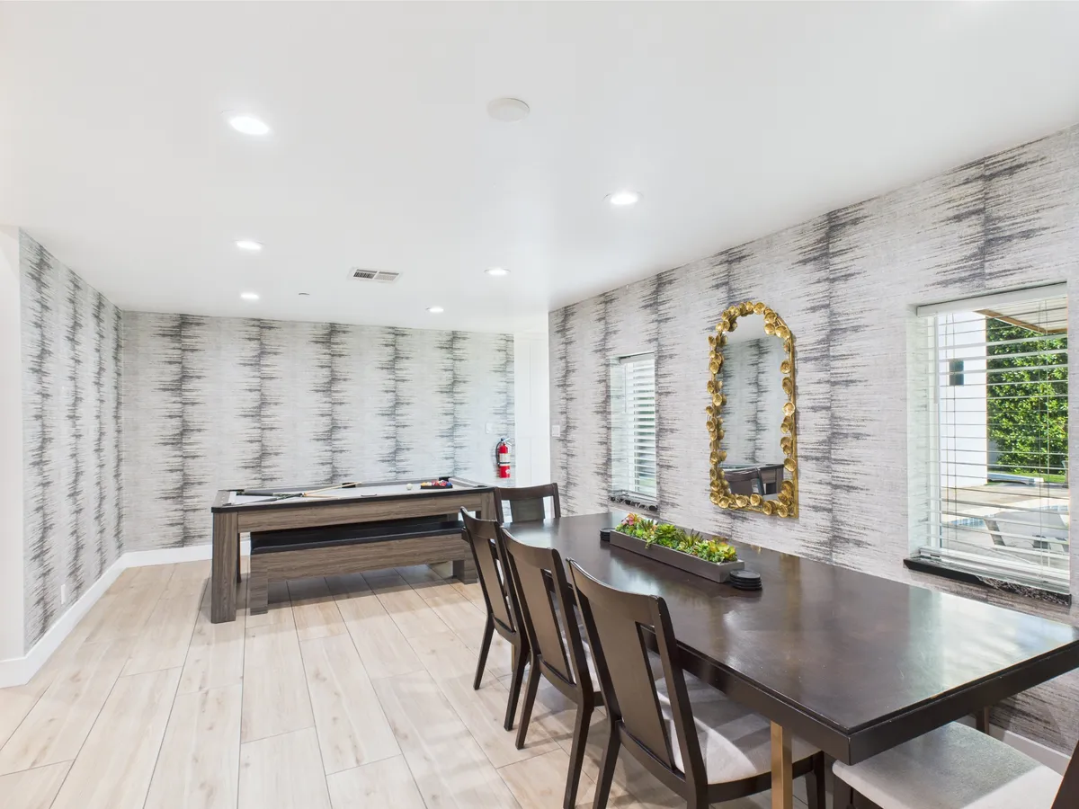 A spacious dining room with a large table set beneath a decorative mirror and textured wall. The table is ready for family meals or memorable group celebrations, with enough seating to accommodate larger parties. The contemporary decor and welcoming layout suggest a space designed for connection and shared meals.