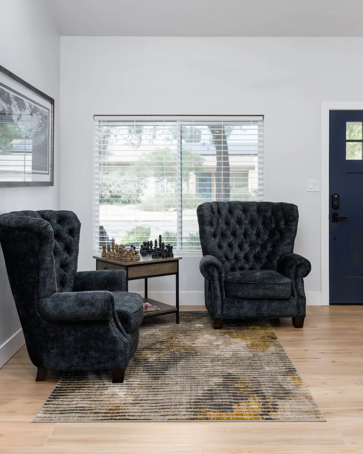 A relaxed yet elegant interior featuring tufted armchairs positioned around a dedicated chess table, with a generous window view letting in natural light. The arrangement encourages intimate conversations and leisurely chess matches, embodying a sense of both comfort and sophistication.